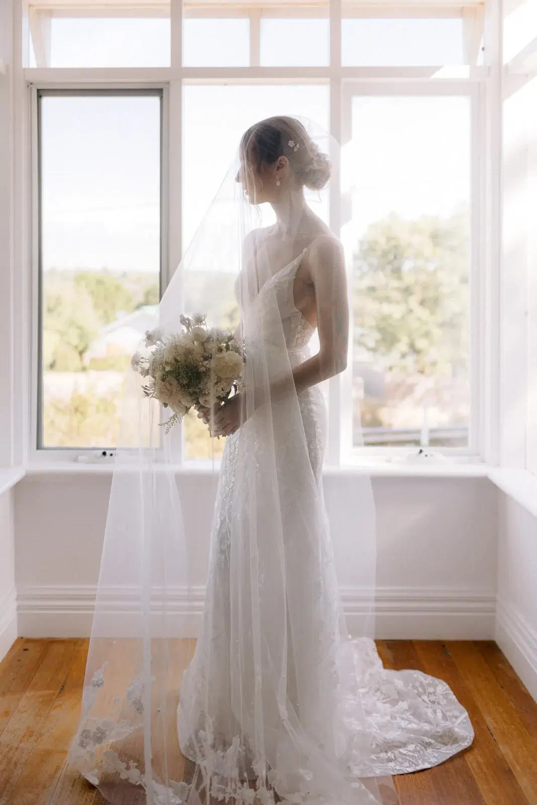 Bride holding a bouquet beside a softly lit window